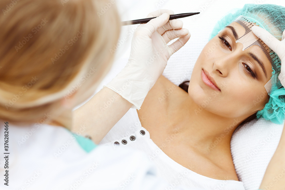 Professional beautician is going to correct eyebrow line at woman face using cosmetic ruler. Permanent brow makeup in beauty salon, closeup. Cosmetology treatment Professional beautician is going to correct eyebrow line at woman face using cosmetic ruler. Permanent brow makeup in beauty salon, closeup. Cosmetology treatment
