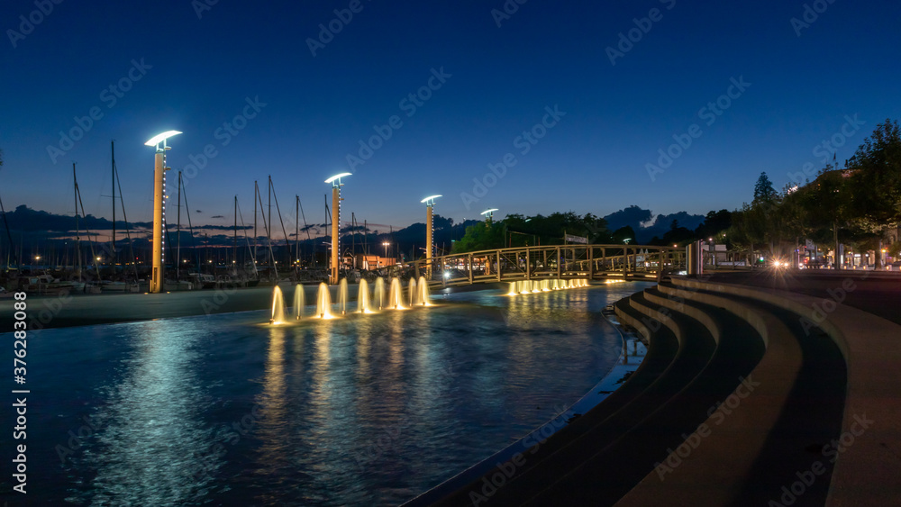 Beautiful night view of fountains, streetlamps at port of Ouchy, Lausanne, Switzerland. Landscape and reflection in water.