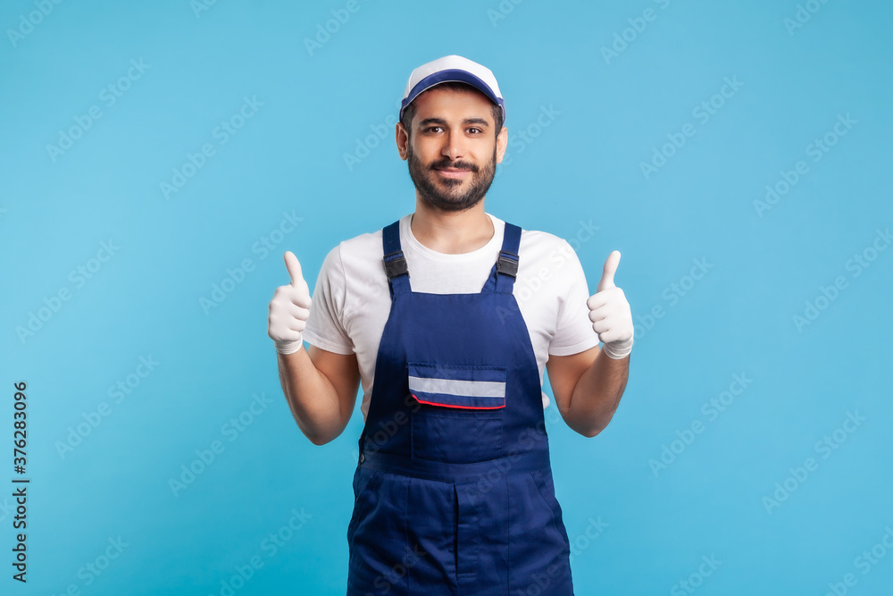 Happy satisfied handyman in overalls and hygiene gloves showing thumbs up, profession of service industry, courier delivery, housekeeping maintenance. Worker in uniform gesturing like. studio shot Happy satisfied handyman in overalls and hygiene gloves showing thumbs up, profession of service industry, courier delivery, housekeeping maintenance. Worker in uniform gesturing like. studio shot