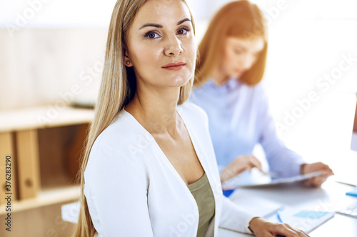 Business woman portrait at sunny office. Businesspeople or colleagues discussing something at meeting while sitting at the desk in office. Casual clothes style. Audit, tax or lawyer concept