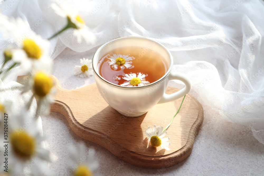 Chamomile tea in a white Cup on a wooden Board on a background of a delicate white napkin, close-up, side view, bokeh Chamomile tea in a white Cup on a wooden Board on a background of a delicate white napkin, close-up, side view, bokeh