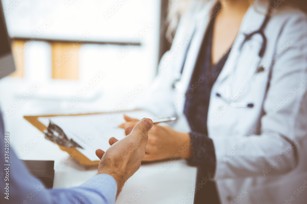 Fototapeta premium Female doctor and male patient discussing current health examination while sitting in clinic, close-up. Medicine concept