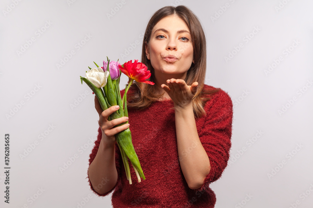 Portrait of beautiful girl holding bouquet of tulips, sending sensual air kiss, expressing love feelings on romantic date, enjoying spring flowers. indoor studio shot isolated on gray background Portrait of beautiful girl holding bouquet of tulips, sending sensual air kiss, expressing love feelings on romantic date, enjoying spring flowers. indoor studio shot isolated on gray background