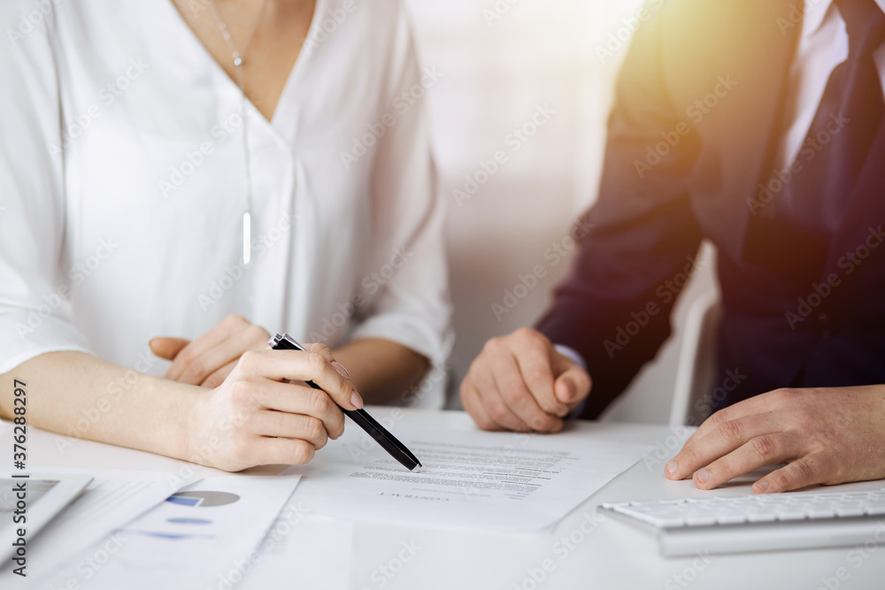 Unknown businessman and woman discussing contract in sunny office, close-up.Business people or lawyers working together at meeting Unknown businessman and woman discussing contract in sunny office, close-up.Business people or lawyers working together at meeting