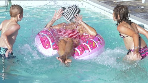 rother and sister have fun in the pool splashing their mom with water photo