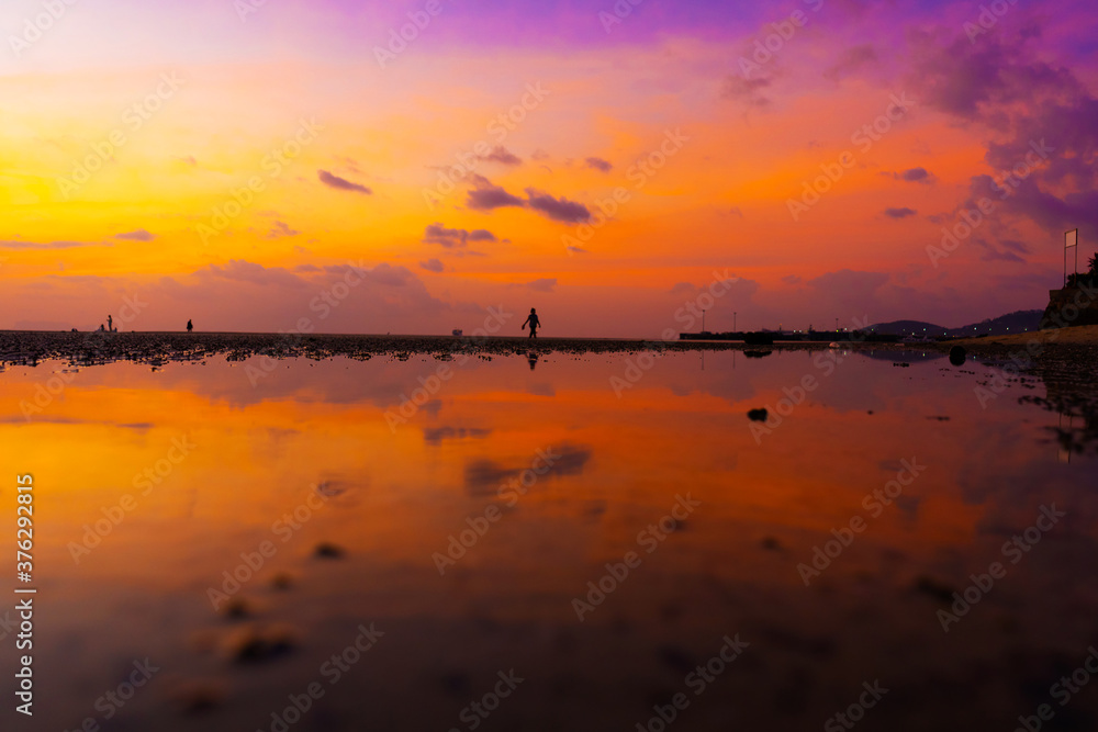 Burning bright sky during sunset on a tropical beach. Sunset during the exodus, the strength of people walking on water Burning bright sky during sunset on a tropical beach. Sunset during the exodus, the strength of people walking on water