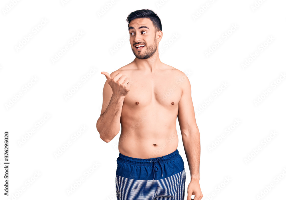 Fototapeta premium Young handsome man wearing swimwear smiling with happy face looking and pointing to the side with thumb up.