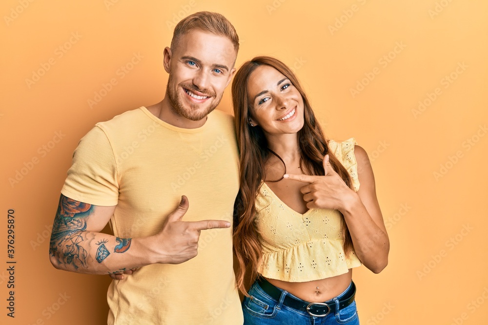 Young couple of girlfriend and boyfriend hugging and standing together cheerful with a smile on face pointing with hand and finger up to the side with happy and natural expression Young couple of girlfriend and boyfriend hugging and standing together cheerful with a smile on face pointing with hand and finger up to the side with happy and natural expression