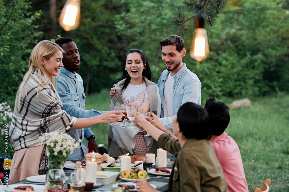 Fototapeta premium Three happy young restful couples sitting by served table in natural environment