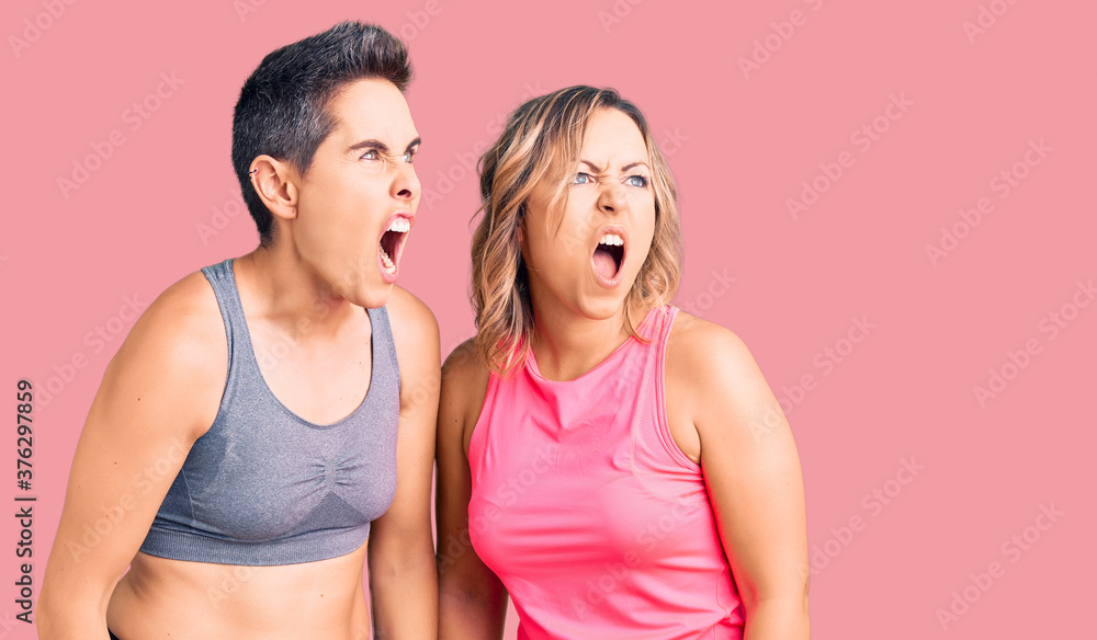 Couple of women wearing sportswear angry and mad screaming frustrated and furious, shouting with anger. rage and aggressive concept.