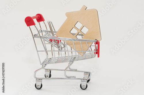 a small wooden house with a window, lies on a trolley from a supermarket, on a white background. Concept - purchase, acquisition, real estate, affordable housing, mortgage. Horizontal photo, close-up.