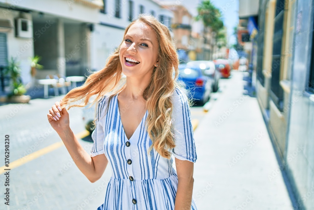Young beautiful caucasian woman with blond hair smiling happy and cheerful walking on sunny day