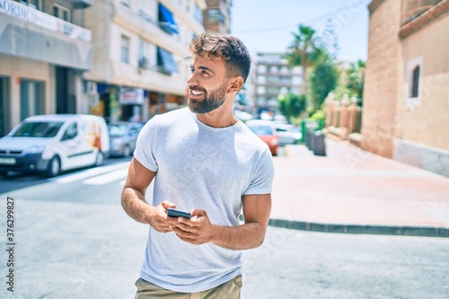Young hispanic man smiling happy using smartphone walking at the cit