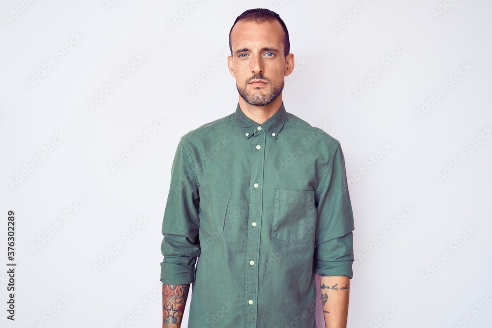 Fototapeta premium Young handsome man with tattoo wearing casual clothes with serious expression on face. simple and natural looking at the camera.