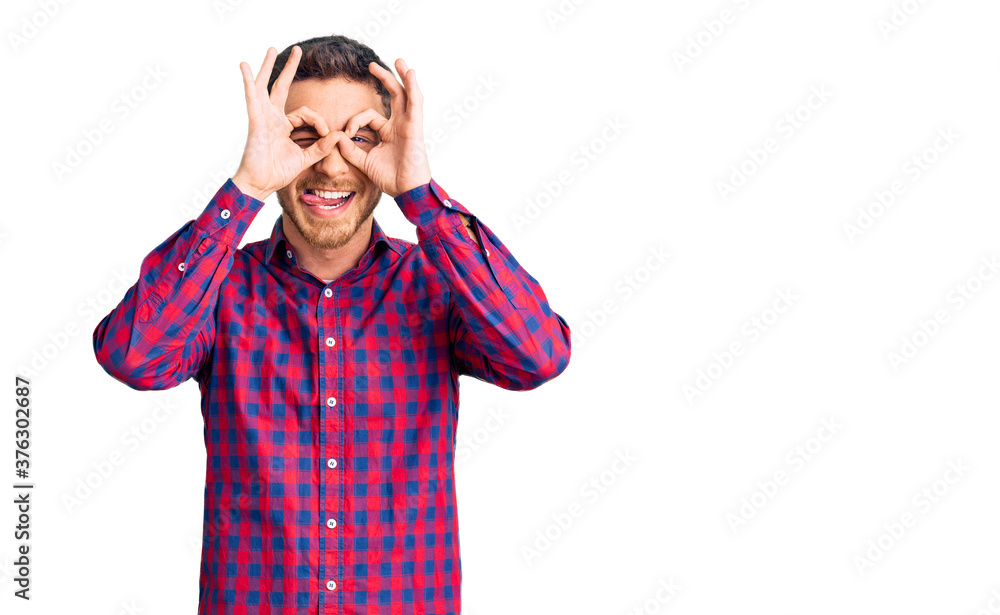 Handsome young man with bear wearing casual shirt doing ok gesture like binoculars sticking tongue out, eyes looking through fingers. crazy expression. Handsome young man with bear wearing casual shirt doing ok gesture like binoculars sticking tongue out, eyes looking through fingers. crazy expression.