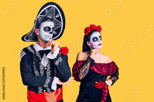 Young couple wearing mexican day of the dead costume over background with hand on chin thinking about question, pensive expression. smiling with thoughtful face. doubt concept.