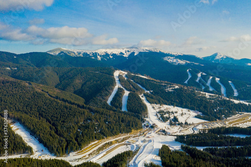 Aerial view of landscape of ski and snowboard slopes through pine trees going down to winter resort in Carpathians