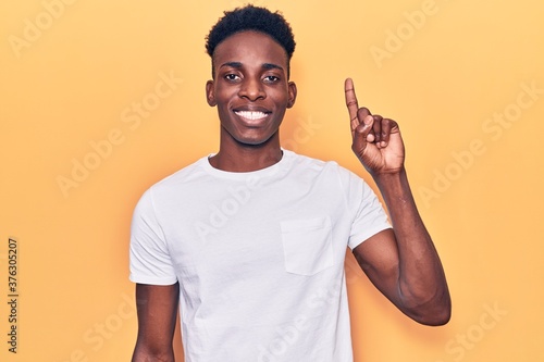 Young african american man wearing casual clothes showing and pointing up with finger number one while smiling confident and happy.