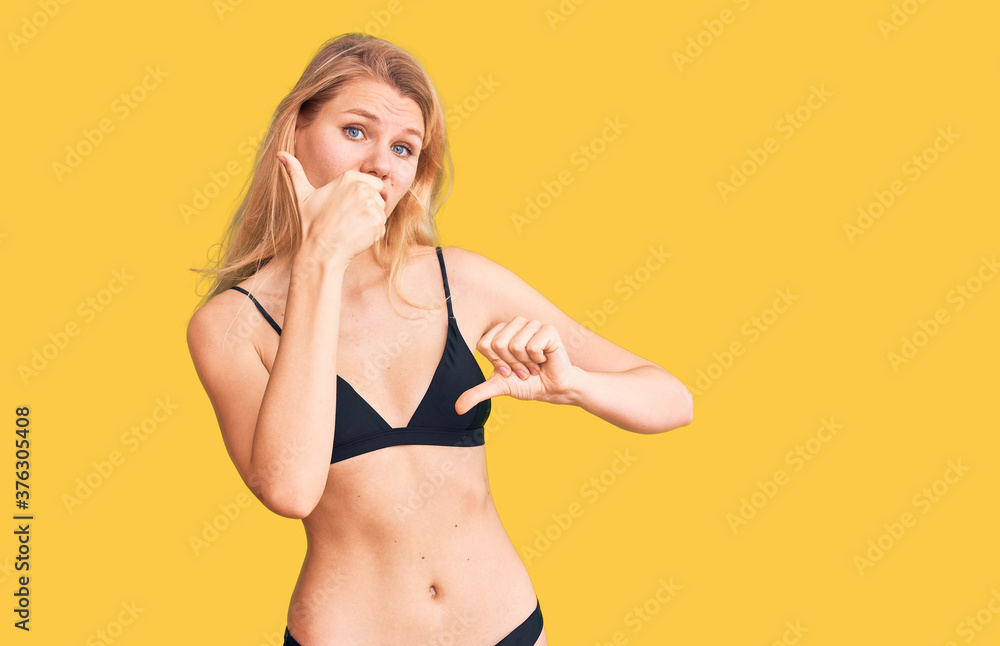 Fototapeta premium Young beautiful blonde woman wearing bikini doing thumbs up and down, disagreement and agreement expression. crazy conflict