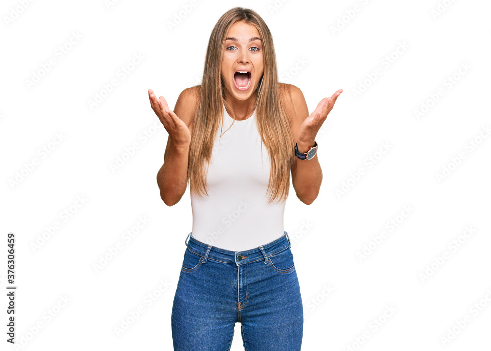 Young blonde woman wearing casual style with sleeveless shirt celebrating mad and crazy for success with arms raised and closed eyes screaming excited. winner concept Young blonde woman wearing casual style with sleeveless shirt celebrating mad and crazy for success with arms raised and closed eyes screaming excited. winner concept