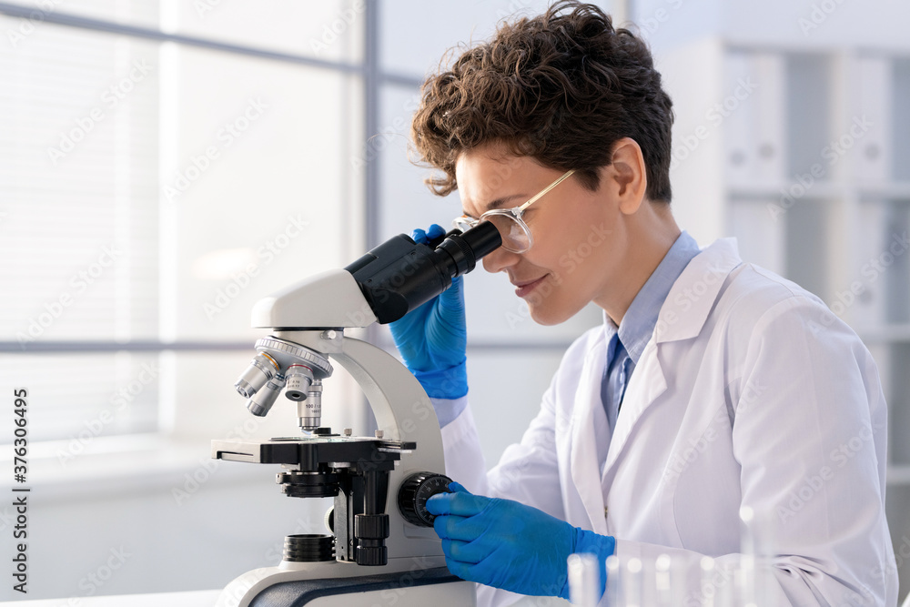 Young woman looking in microscope while studying new chemical substances Young woman looking in microscope while studying new chemical substances