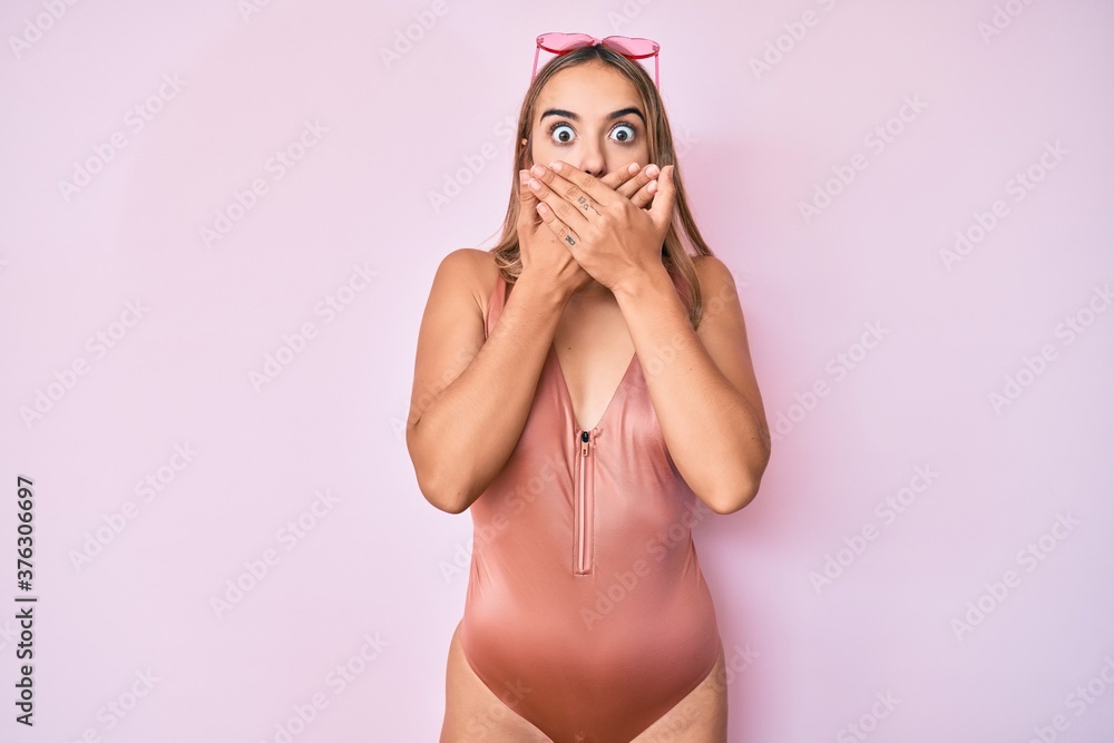 Young beautiful blonde woman wearing swimsuit and sunglasses shocked covering mouth with hands for mistake. secret concept. Young beautiful blonde woman wearing swimsuit and sunglasses shocked covering mouth with hands for mistake. secret concept.