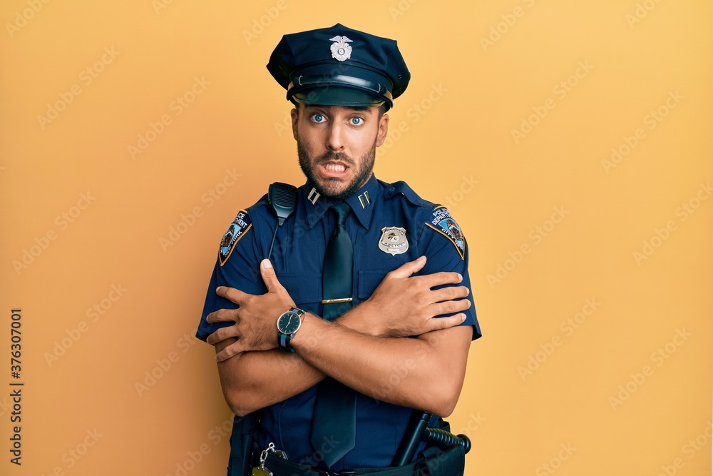 Handsome hispanic man wearing police uniform shaking and freezing for winter cold with sad and shock expression on face