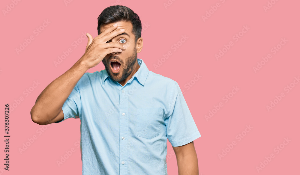 Handsome hispanic man wearing casual clothes peeking in shock covering face and eyes with hand, looking through fingers with embarrassed expression. Handsome hispanic man wearing casual clothes peeking in shock covering face and eyes with hand, looking through fingers with embarrassed expression.