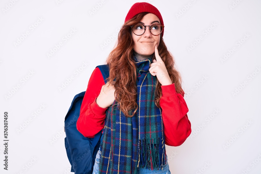 Young beautiful woman wearing winter scarf and student backpack serious face thinking about question with hand on chin, thoughtful about confusing idea Young beautiful woman wearing winter scarf and student backpack serious face thinking about question with hand on chin, thoughtful about confusing idea