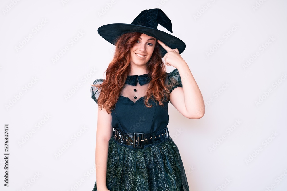 Young beautiful woman wearing witch halloween costume smiling pointing to head with one finger, great idea or thought, good memory