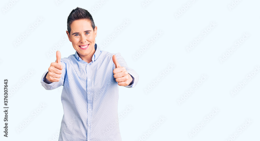 Young woman with short hair wearing business clothes approving doing positive gesture with hand, thumbs up smiling and happy for success. winner gesture. Young woman with short hair wearing business clothes approving doing positive gesture with hand, thumbs up smiling and happy for success. winner gesture.