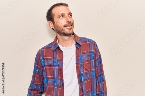Young handsome man wearing casual clothes looking away to side with smile on face, natural expression. laughing confident.