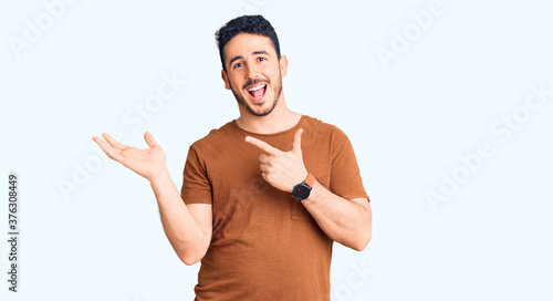 Young hispanic man wearing casual clothes amazed and smiling to the camera while presenting with hand and pointing with finger.