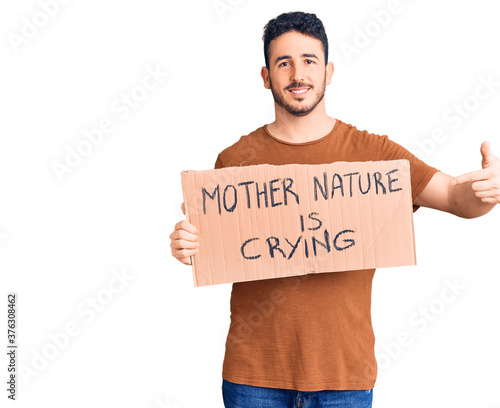 Wallpaper Mural Young hispanic man holding mother nature is crying protest cardboard banner smiling happy pointing with hand and finger Torontodigital.ca
