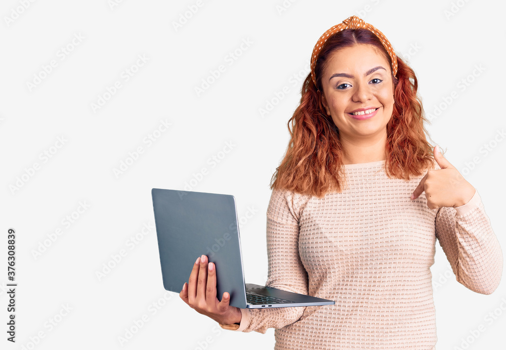Young latin woman holding laptop pointing finger to one self smiling happy and proud Young latin woman holding laptop pointing finger to one self smiling happy and proud