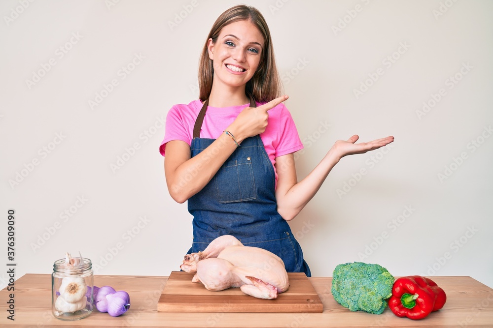 Young blonde girl wearing cook apron and holding chicken amazed and smiling to the camera while presenting with hand and pointing with finger. Young blonde girl wearing cook apron and holding chicken amazed and smiling to the camera while presenting with hand and pointing with finger.