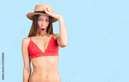 Beautiful brunette young woman wearing bikini surprised with hand on head for mistake, remember error. forgot, bad memory concept.