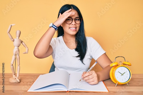 Young beautiful asian girl sitting on the table stuying for university stressed and frustrated with hand on head, surprised and angry face photo