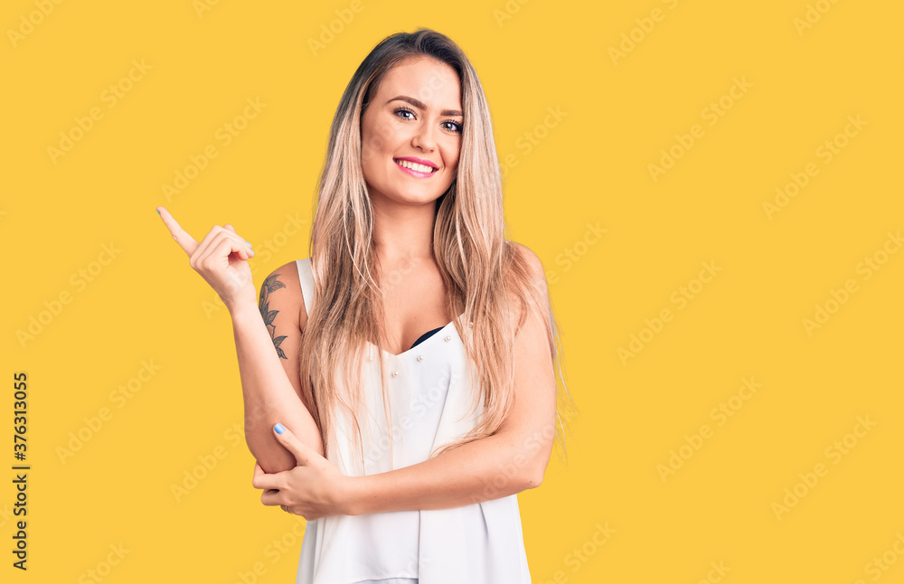 Young beautiful blonde woman wearing sleeveless t-shirt smiling happy pointing with hand and finger to the side Young beautiful blonde woman wearing sleeveless t-shirt smiling happy pointing with hand and finger to the side