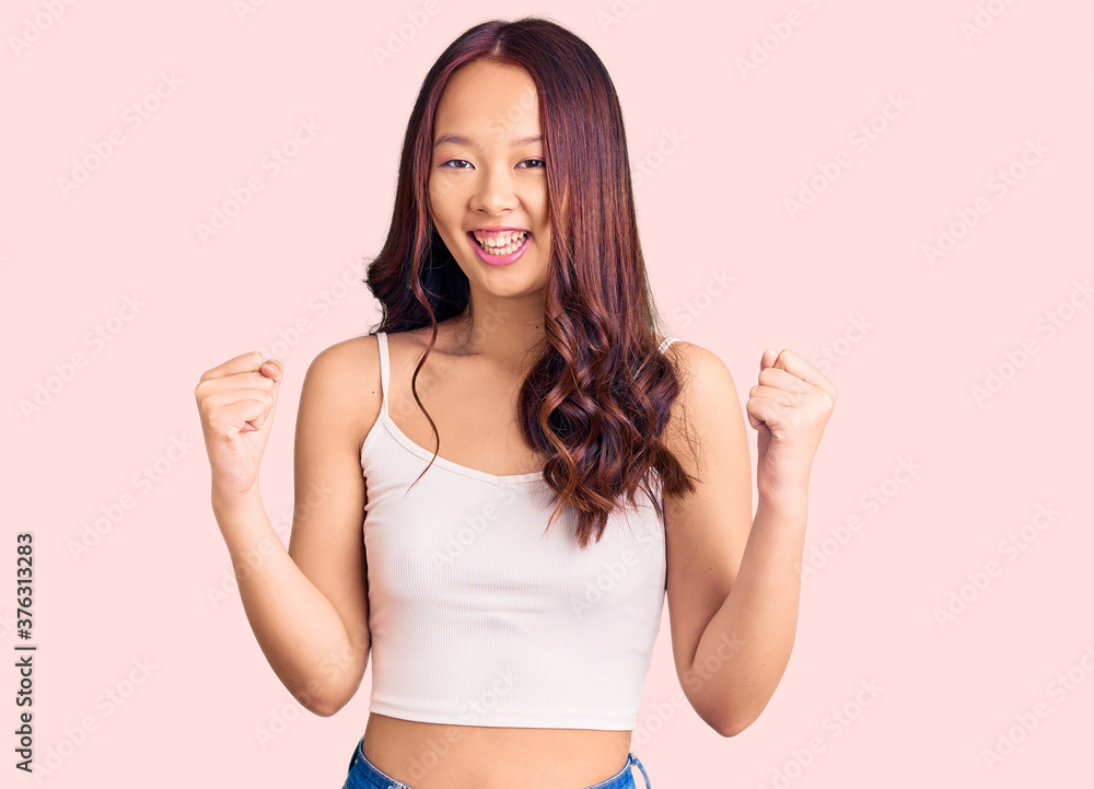 Young beautiful chinese girl wearing casual clothes celebrating surprised and amazed for success with arms raised and open eyes. winner concept. Young beautiful chinese girl wearing casual clothes celebrating surprised and amazed for success with arms raised and open eyes. winner concept.