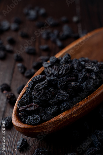 Close up of black raisins in a wooden bowl, close up, dark background, studio photo with soft light