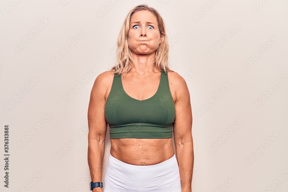 Middle age caucasian blonde woman wearing sportswear puffing cheeks with funny face. mouth inflated with air, crazy expression. Middle age caucasian blonde woman wearing sportswear puffing cheeks with funny face. mouth inflated with air, crazy expression.