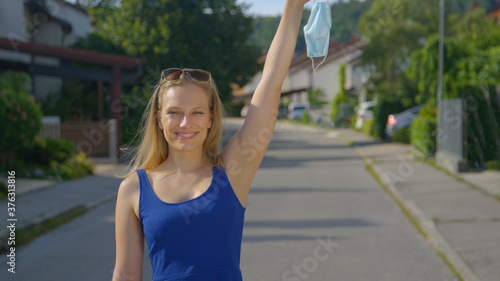 PORTRAT: Cheerful young Caucasian woman lifts her surgical mask above her head.