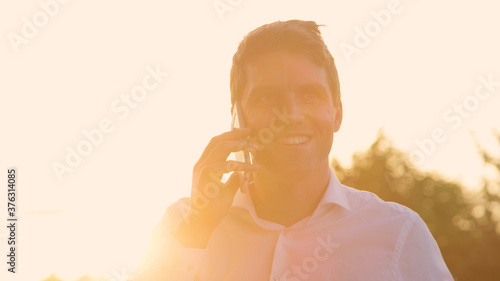 CLOSE UP: Successful businessman talks on the phone at golden summer sunset.