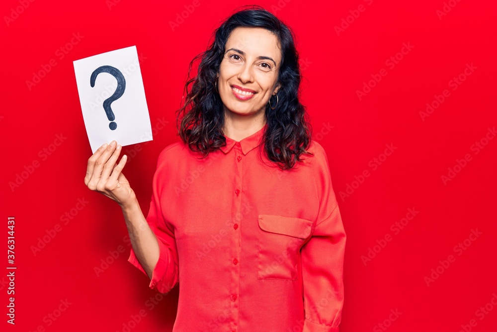 Young beautiful hispanic woman holding question mark looking positive and happy standing and smiling with a confident smile showing teeth Young beautiful hispanic woman holding question mark looking positive and happy standing and smiling with a confident smile showing teeth