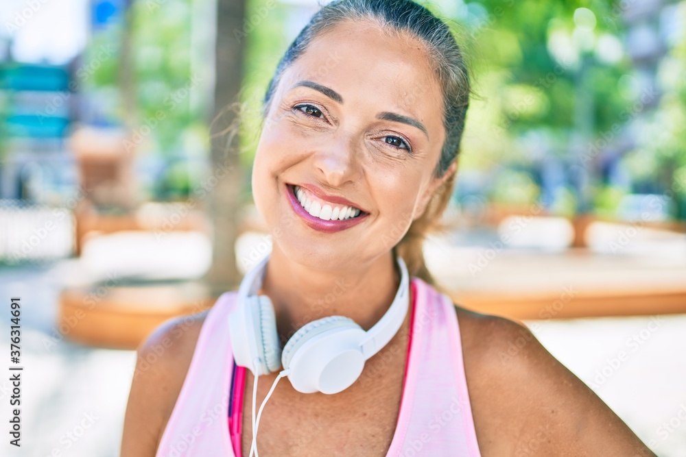 Middle age sportswoman smiling happy  wearing headphones at the park
