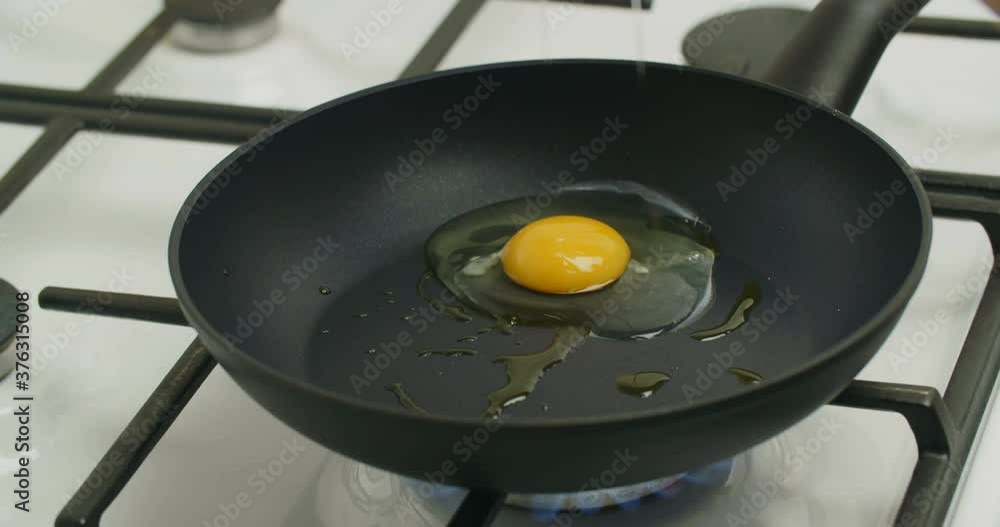 A woman breaks and fries two eggs in a pan on a gas stove. A woman breaks and fries two eggs in a pan on a gas stove.