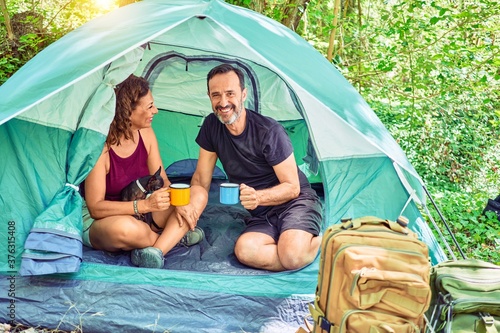 Middle age couple of hiker smiling happy looking at the camera. Drinking coffee camping at the forest.