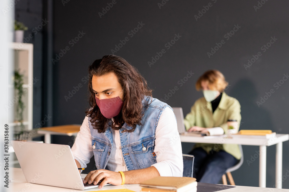 Young serious businessman in casualwear and protective mask working in the net