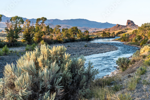 Rock outcropping over the river with trees and shrub on the banks and mountain in the background, South Fork Shoshone River, Cody, Wyoming photo